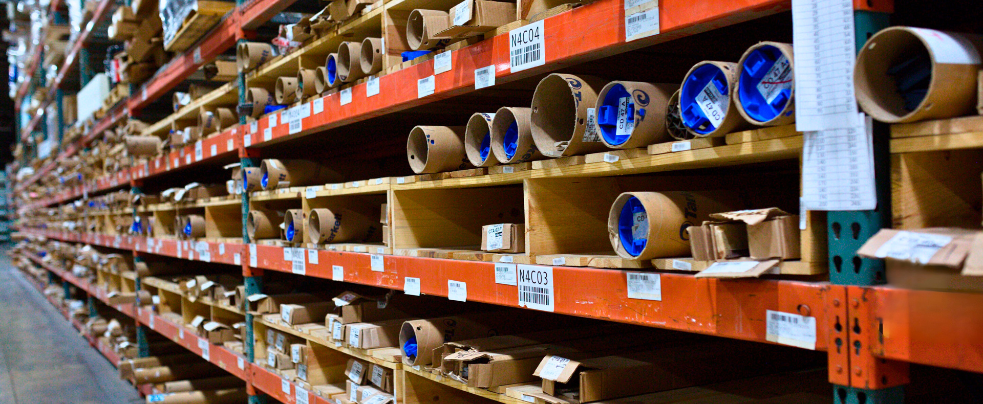Warehouse shelves with labeled cardboard tubes and boxes.